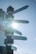 A signpost with directional signs pointing towards cities such as Sydney, Amsterdam, London, New Delhi, and New York, each accompanied by its distance in kilometers. Sunlight creates a bright flare effect in the background against a clear blue sky.