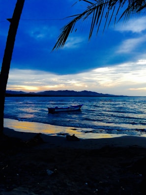 A serene beach with gentle waves and a solitary fisherman’s boat at dusk.