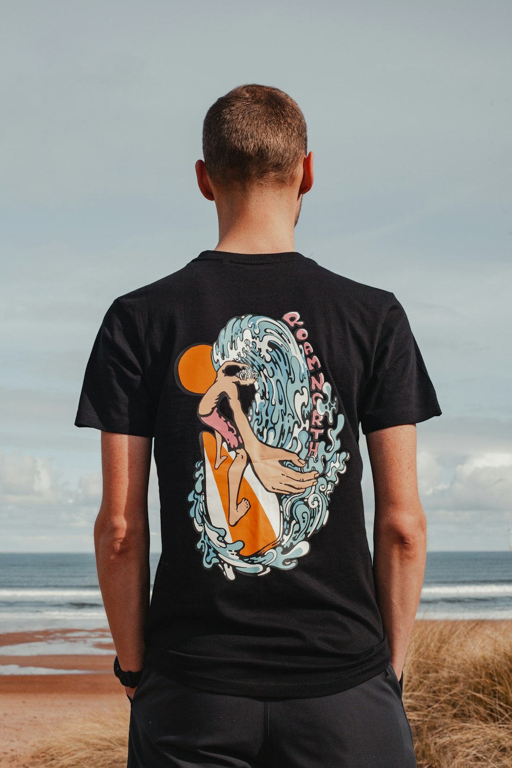 a man standing on a beach wearing a t - shirt with an image of a