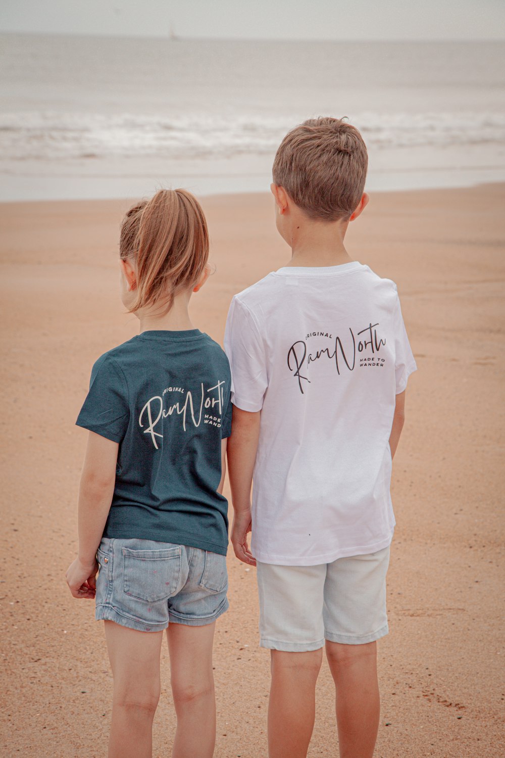 a couple of kids standing on top of a sandy beach