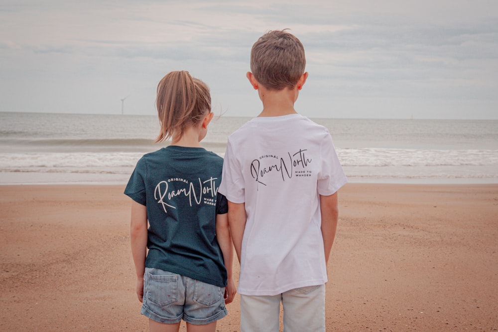 a couple of kids standing on top of a sandy beach