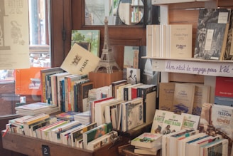 many books are stacked on a table in front of a window