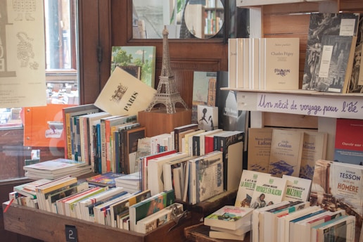 many books are stacked on a table in front of a window