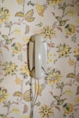Close-up of a retro rotary phone resting on a colorful 1970s floral wallpaper.