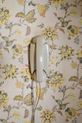 Close-up of a retro rotary phone resting on a colorful 1970s floral wallpaper.