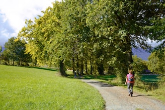 a woman walking down a dirt road next to a lush green field