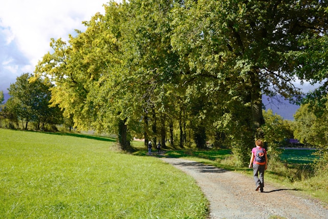 a woman walking down a dirt road next to a lush green field