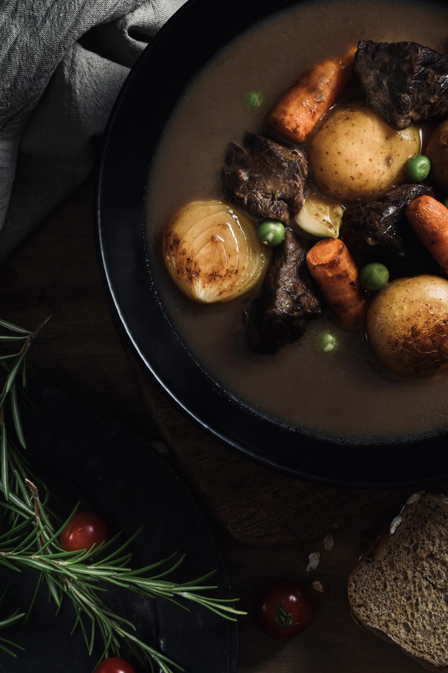 Overhead view of a bowl of beef stew with potatoes, carrots, onion and peas on a dark table