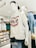 A mannequin wearing a white T-shirt with 'Brillo' written in red and blue text, combined with a pair of blue jeans. The mannequin is also wearing a black baseball cap backwards and white over-ear headphones. Behind it, there's another mannequin with glasses and a shirt, surrounded by neatly folded clothes on shelves.