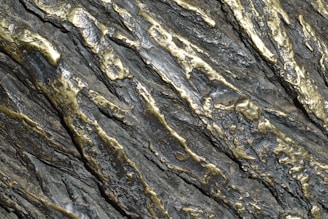 Metallic surface with an intricate pattern of silver and gold tones. The surface has a textured appearance with raised and indented sections, creating a rugged and dynamic visual effect.