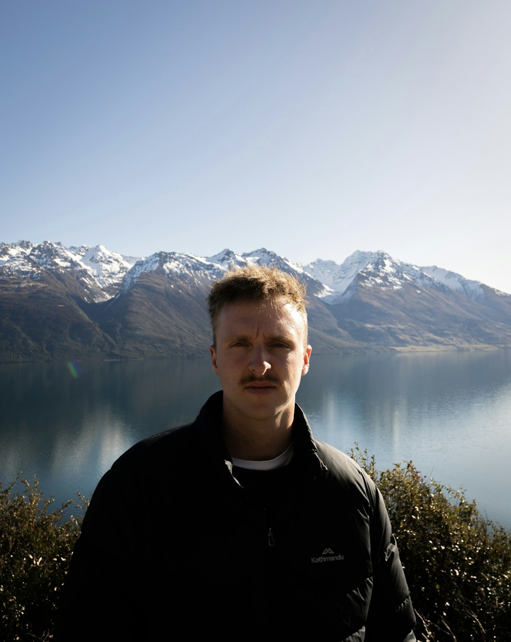 a man standing in front of a lake with mountains in the background
