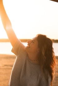 A joyful woman with flowing hair outdoors in soft sunlight.