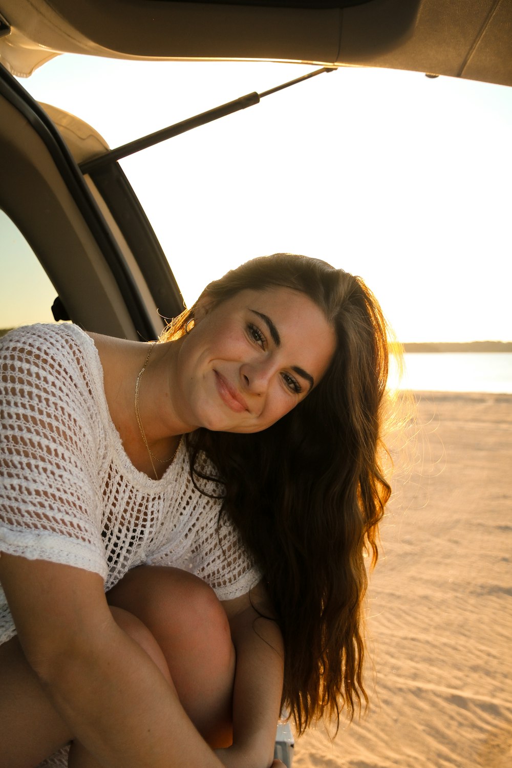 a woman sitting in the back of a car on a beach