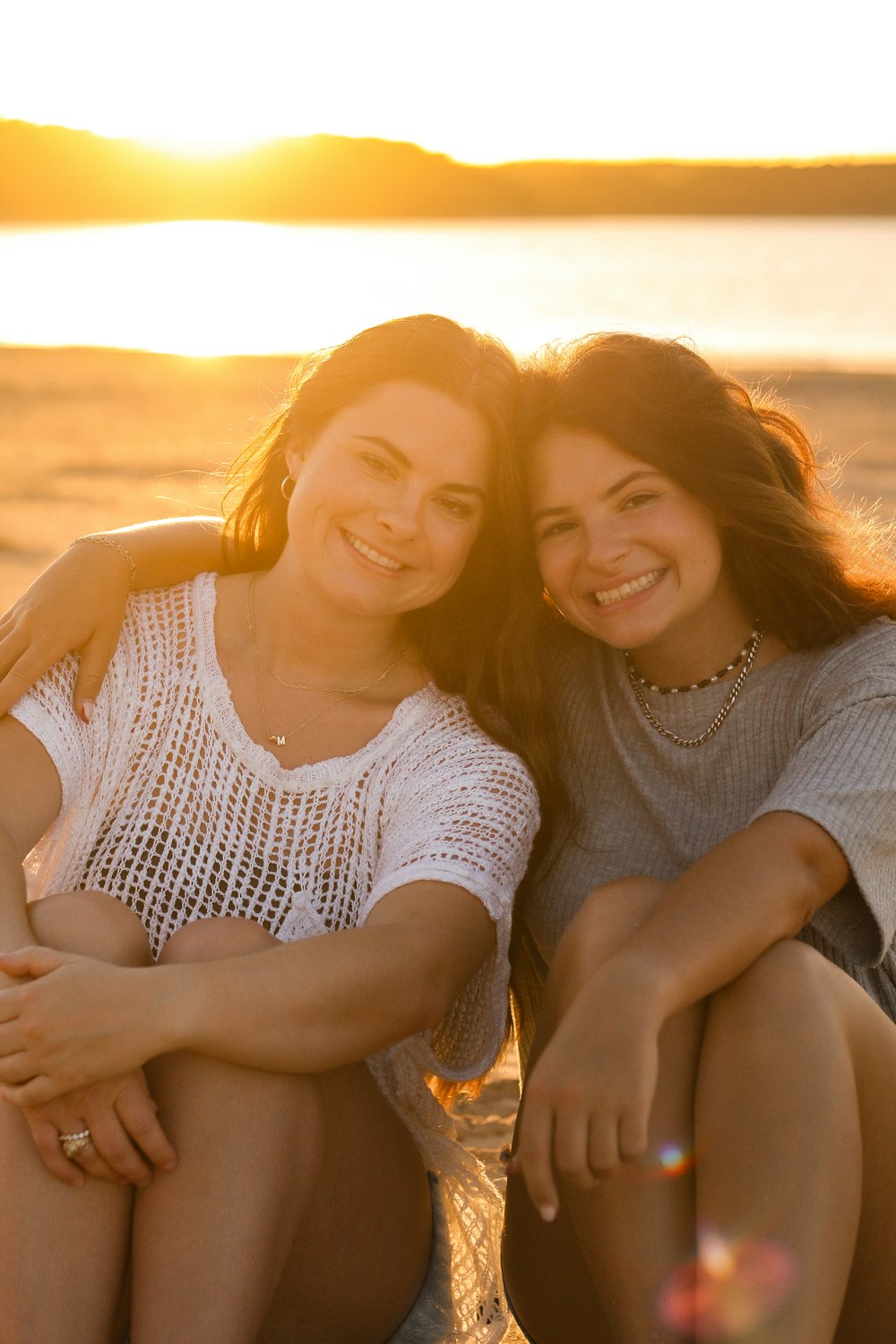 two women sitting next to each other on a beach