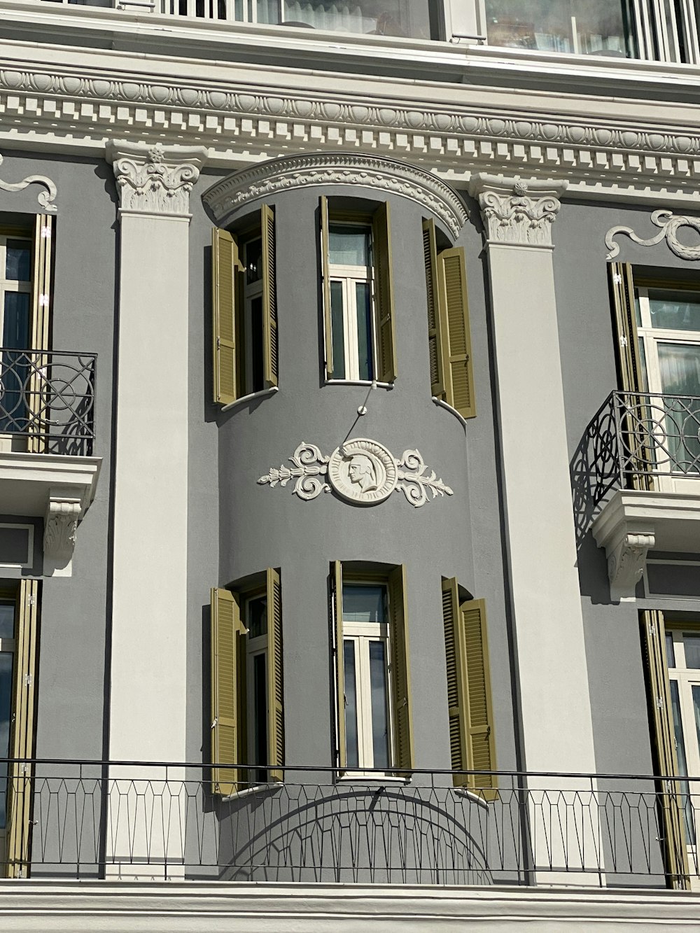 a grey building with yellow shutters and a clock