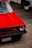 A red vintage car is parked outdoors, showcasing its front hood and bumper. The car features a round headlight and a grill with a GTI emblem. The vehicle has a license plate from Paraguay, reading AUI-680. Potted plants are visible in the background.