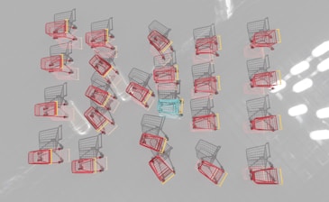 Multiple shopping carts are arranged in a neat pattern on a reflective surface. Most carts are red with one distinct blue cart in the center.