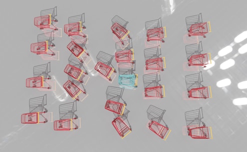 Multiple shopping carts are arranged in a neat pattern on a reflective surface. Most carts are red with one distinct blue cart in the center.