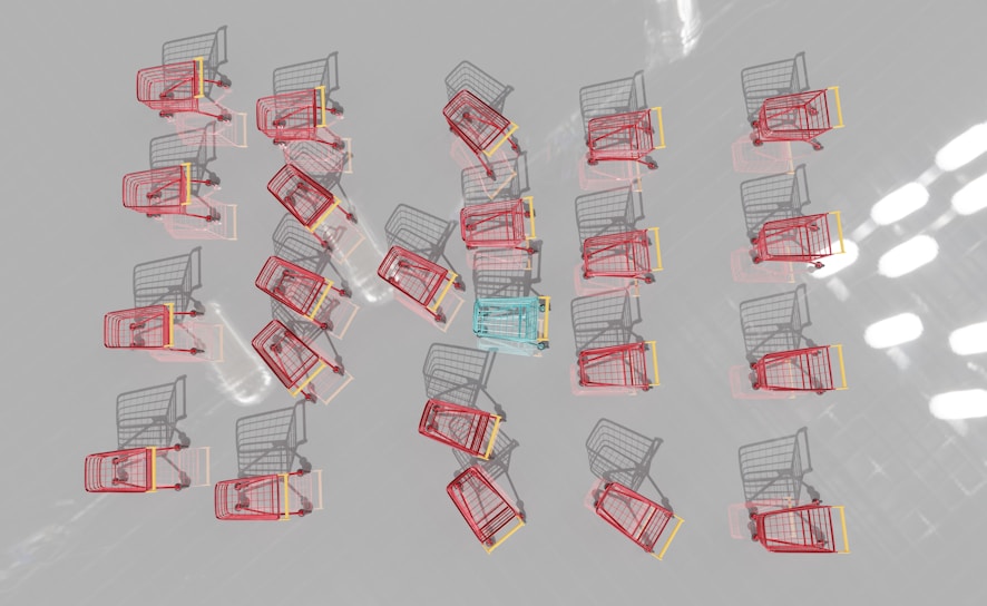 Multiple shopping carts are arranged in a neat pattern on a reflective surface. Most carts are red with one distinct blue cart in the center.