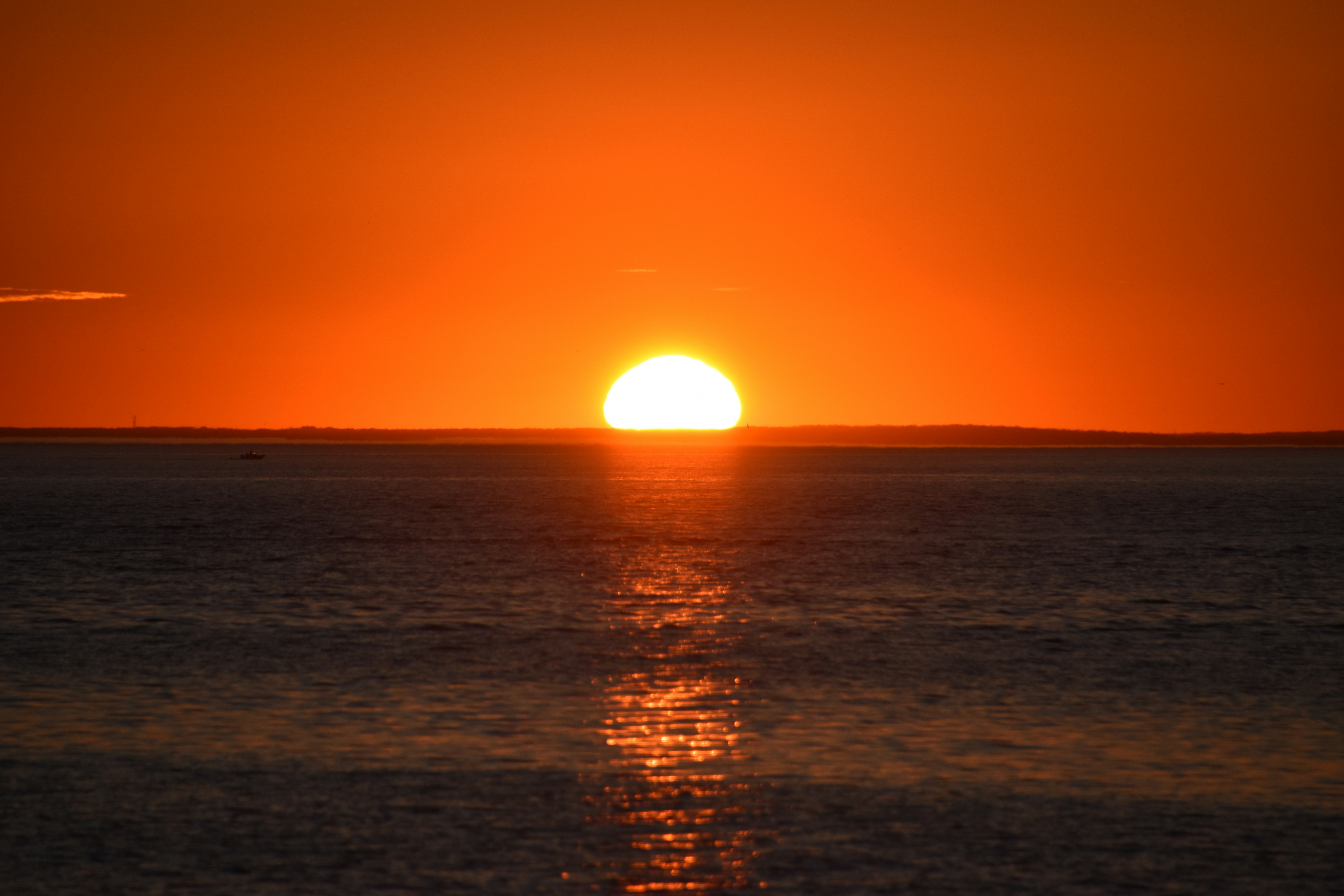 Die Sonne geht über dem Ozean unter, mit einem Boot in der Ferne