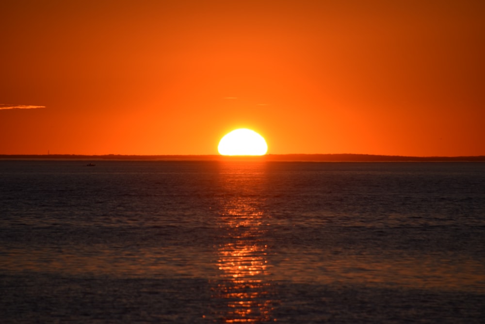 the sun is setting over the ocean with a boat in the distance