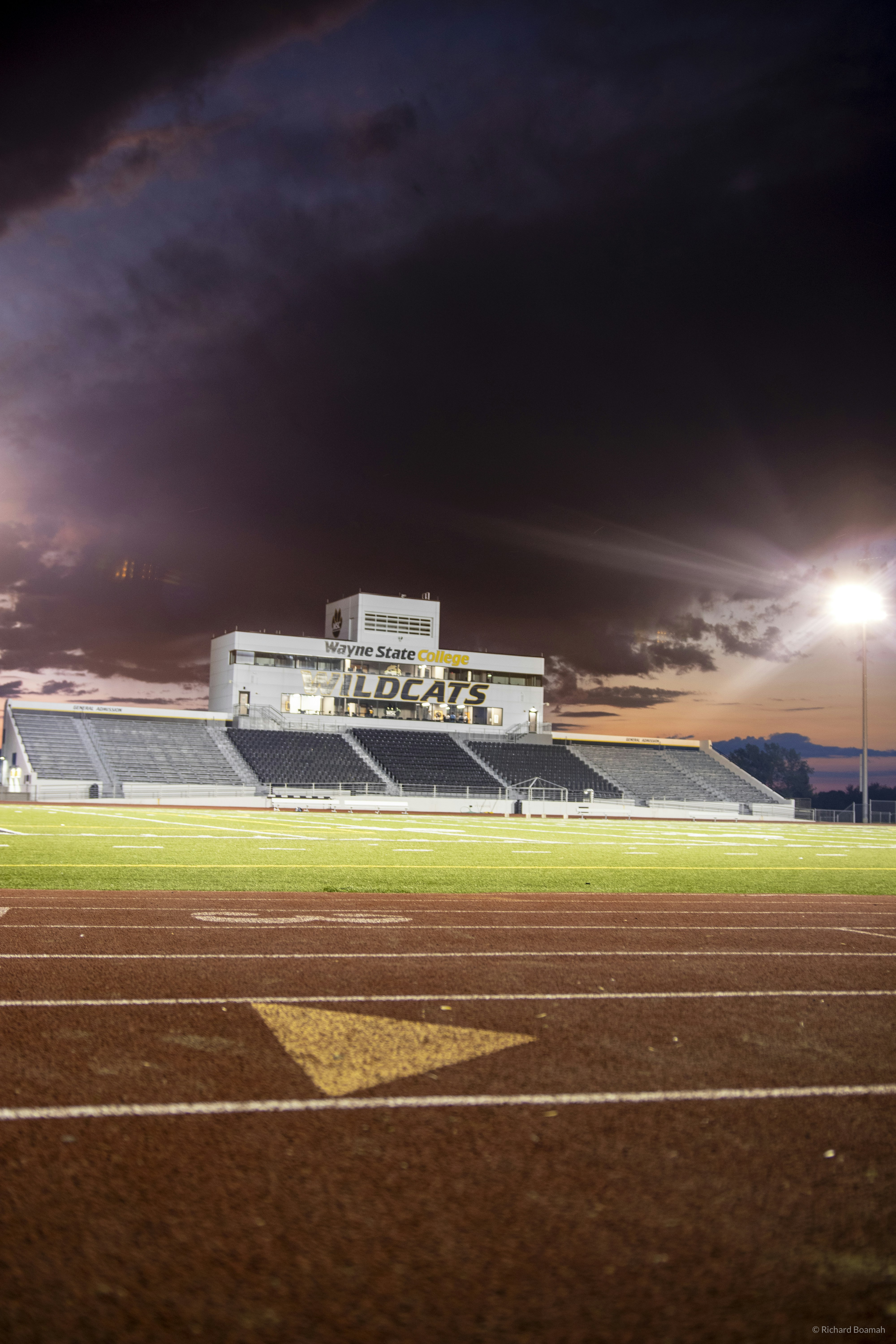 Football pitch at dusk, empty stadium, dramatic floodlights, deep shadows, dark atmospheric