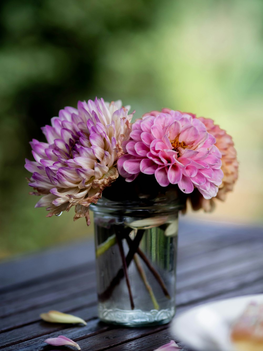 a glass jar filled with pink flowers on top of a wooden table