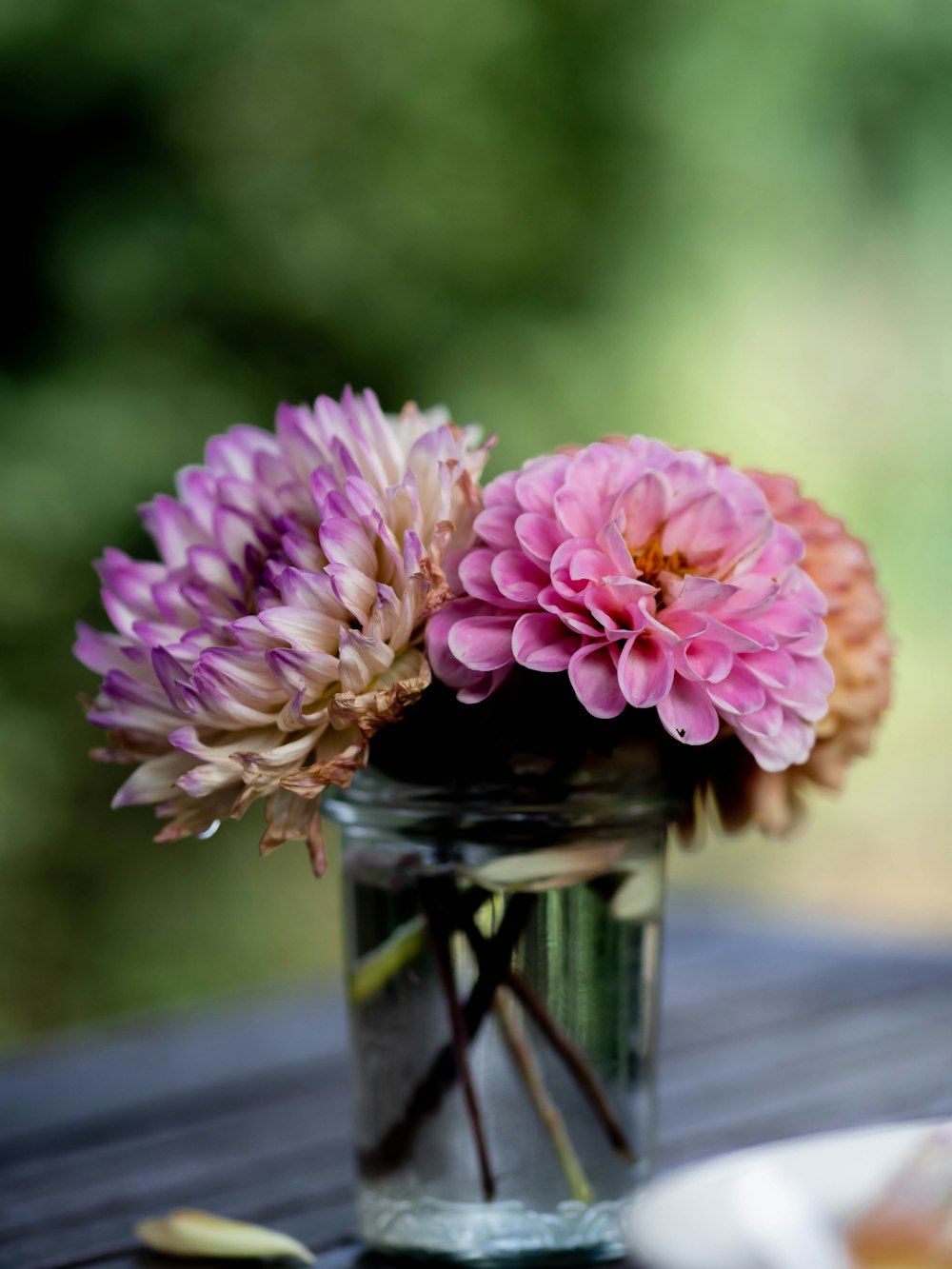 a glass vase filled with pink flowers on top of a wooden table