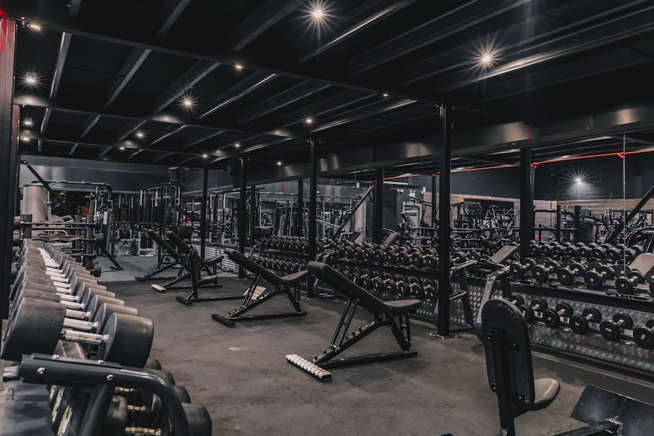 Wide view of a dimly lit gym floor filled with benches, racks, and dumbbells