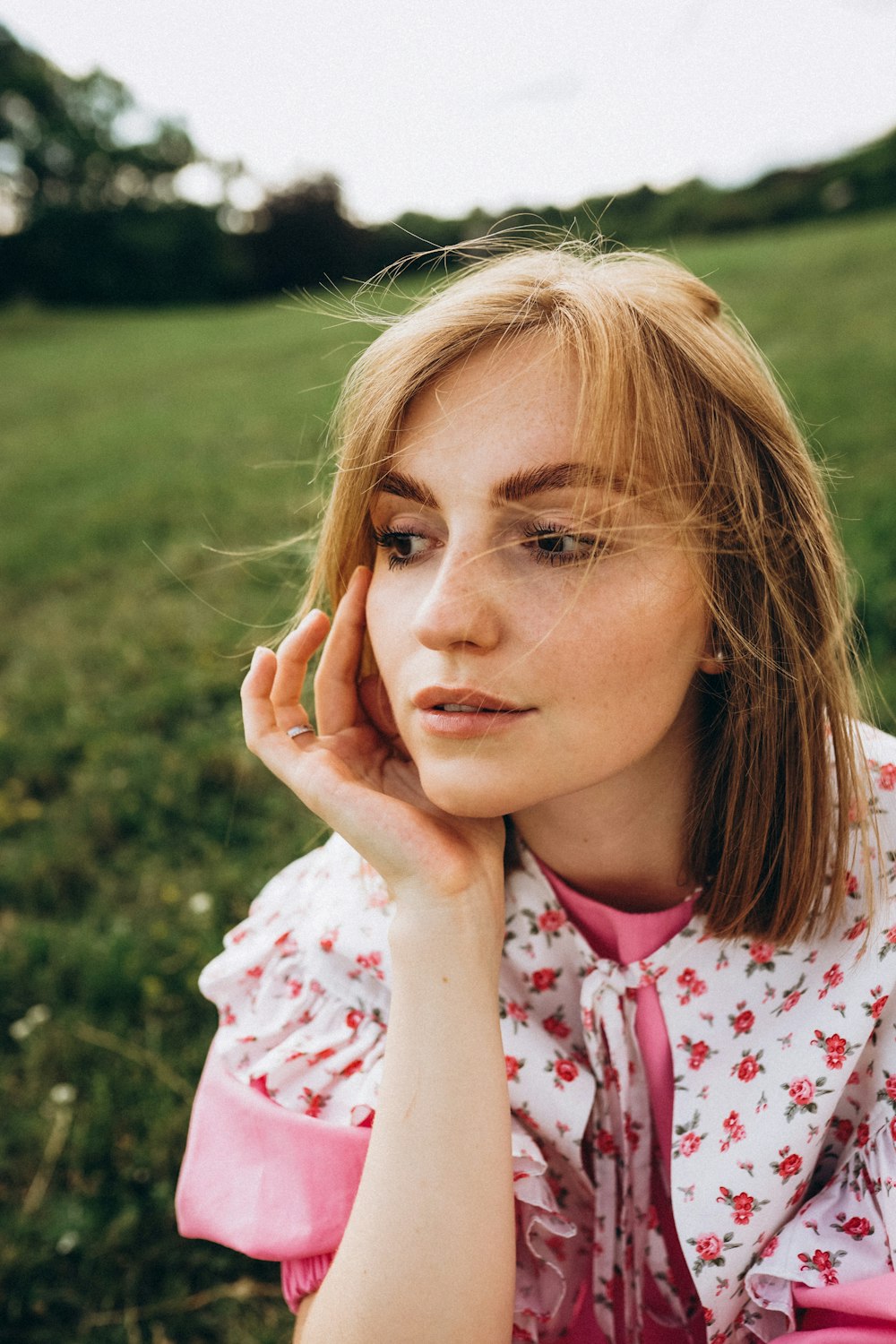 a woman sitting in the grass with her hand on her face