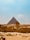 A vast desert landscape with the iconic Great Pyramid of Giza at its center, flanked by the majestic Sphinx in the foreground. Visitors can be seen exploring the ancient monuments under a clear blue sky.