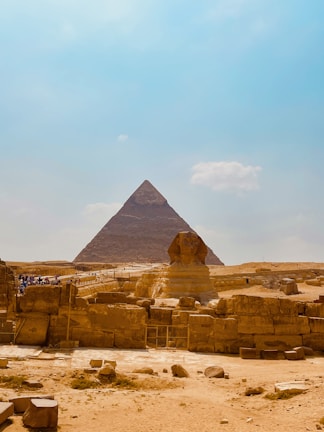 A vast desert landscape with the iconic Great Pyramid of Giza at its center, flanked by the majestic Sphinx in the foreground. Visitors can be seen exploring the ancient monuments under a clear blue sky.
