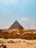 A vast desert landscape with the iconic Great Pyramid of Giza at its center, flanked by the majestic Sphinx in the foreground. Visitors can be seen exploring the ancient monuments under a clear blue sky.