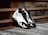A pair of stylish black and white sneakers with red accents is placed on a wooden surface next to a rusty metal railing, creating a contrast between modern fashion and industrial elements.