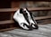 A pair of stylish black and white sneakers with red accents is placed on a wooden surface next to a rusty metal railing, creating a contrast between modern fashion and industrial elements.