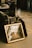 A collection of items is arranged on the floor including a vintage picture frame with a reflective surface, showing an abstract reflection of the surrounding area. Nearby are various objects like records, CDs, a pan, and other miscellaneous items. The scene is set at what appears to be a flea market or garage sale, with people standing in the background.