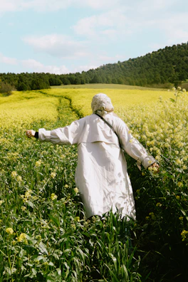 Dilruba Khanam walking through a vibrant mustard field, notebook in hand.
