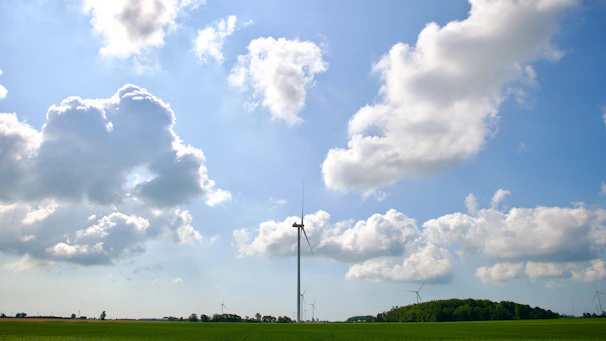 A panoramic view of several white wind turbines spinning gracefully on a sunny day with clear skies.