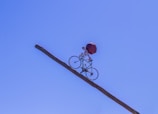 Character balancing on a unicycle on a narrow beam with a bright background.