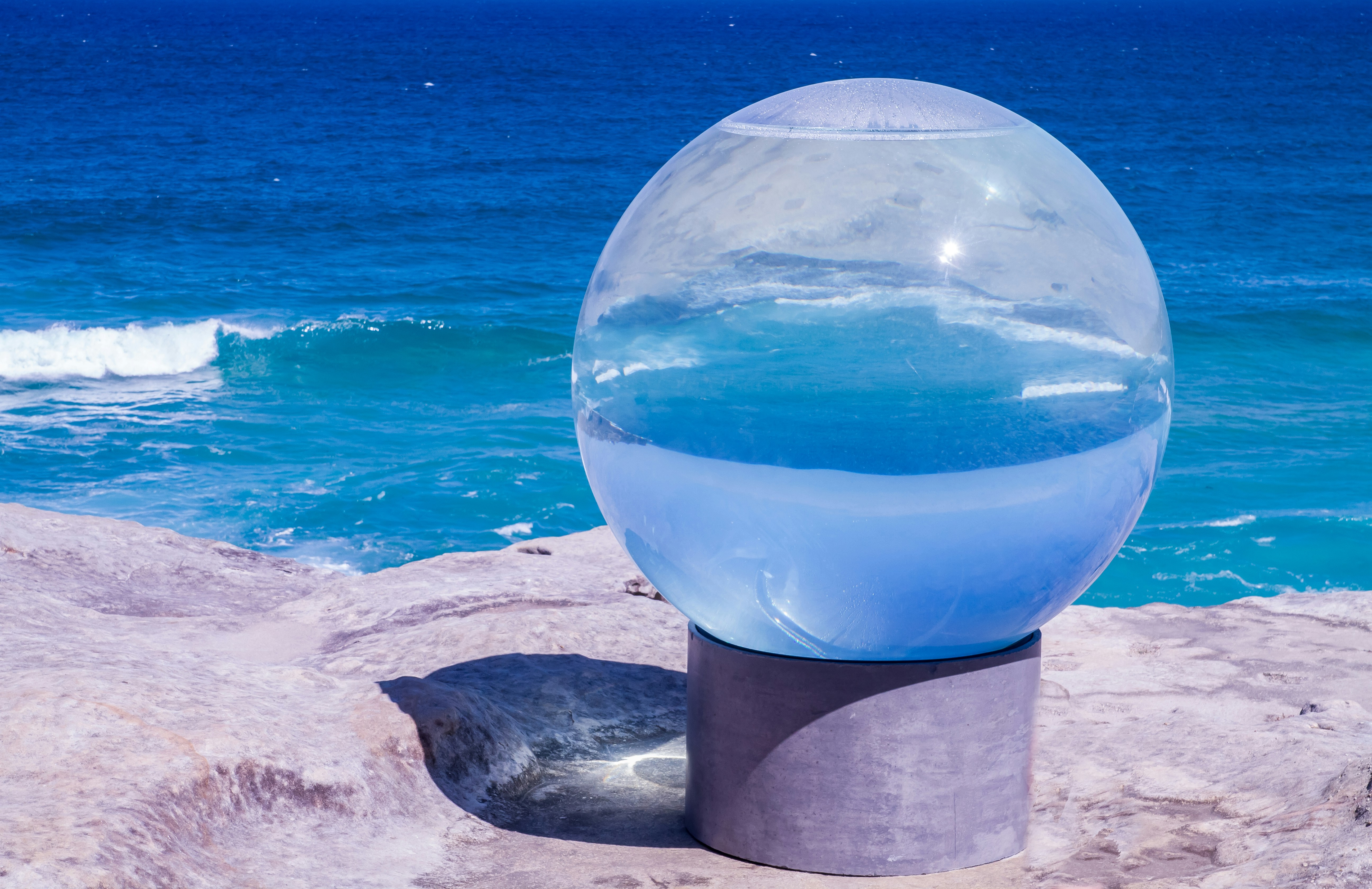 a glass ball sitting on top of a rock near the ocean