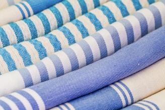 An array of rolled textiles with varying patterns, primarily featuring stripes in shades of blue and white. The fabric textures are visibly detailed, showcasing different weaving styles.