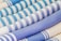 An array of rolled textiles with varying patterns, primarily featuring stripes in shades of blue and white. The fabric textures are visibly detailed, showcasing different weaving styles.