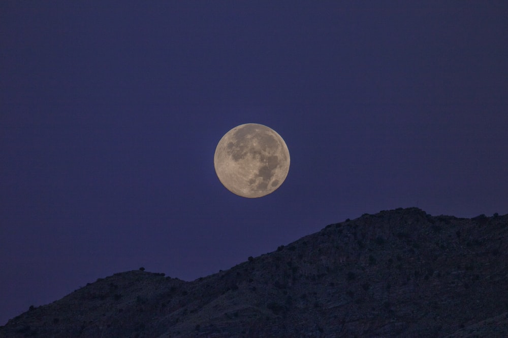 a full moon is seen above a mountain