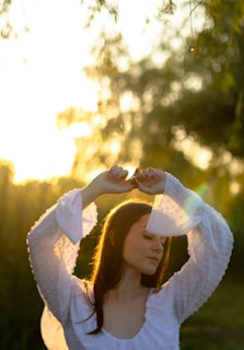 A serene woman standing outdoors with arms raised, basking in soft morning light symbolizing freedom and balance.
