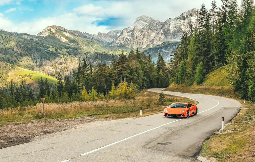 an orange sports car driving down a mountain road