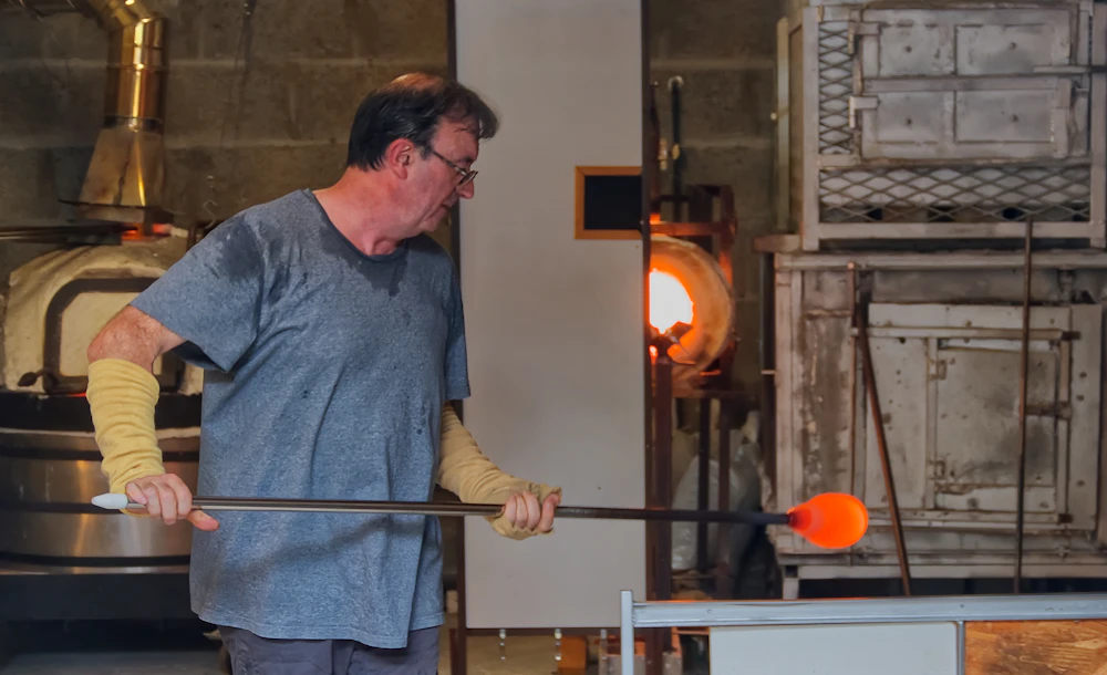 An artist at the furnace, glasses catching the glow of the flame