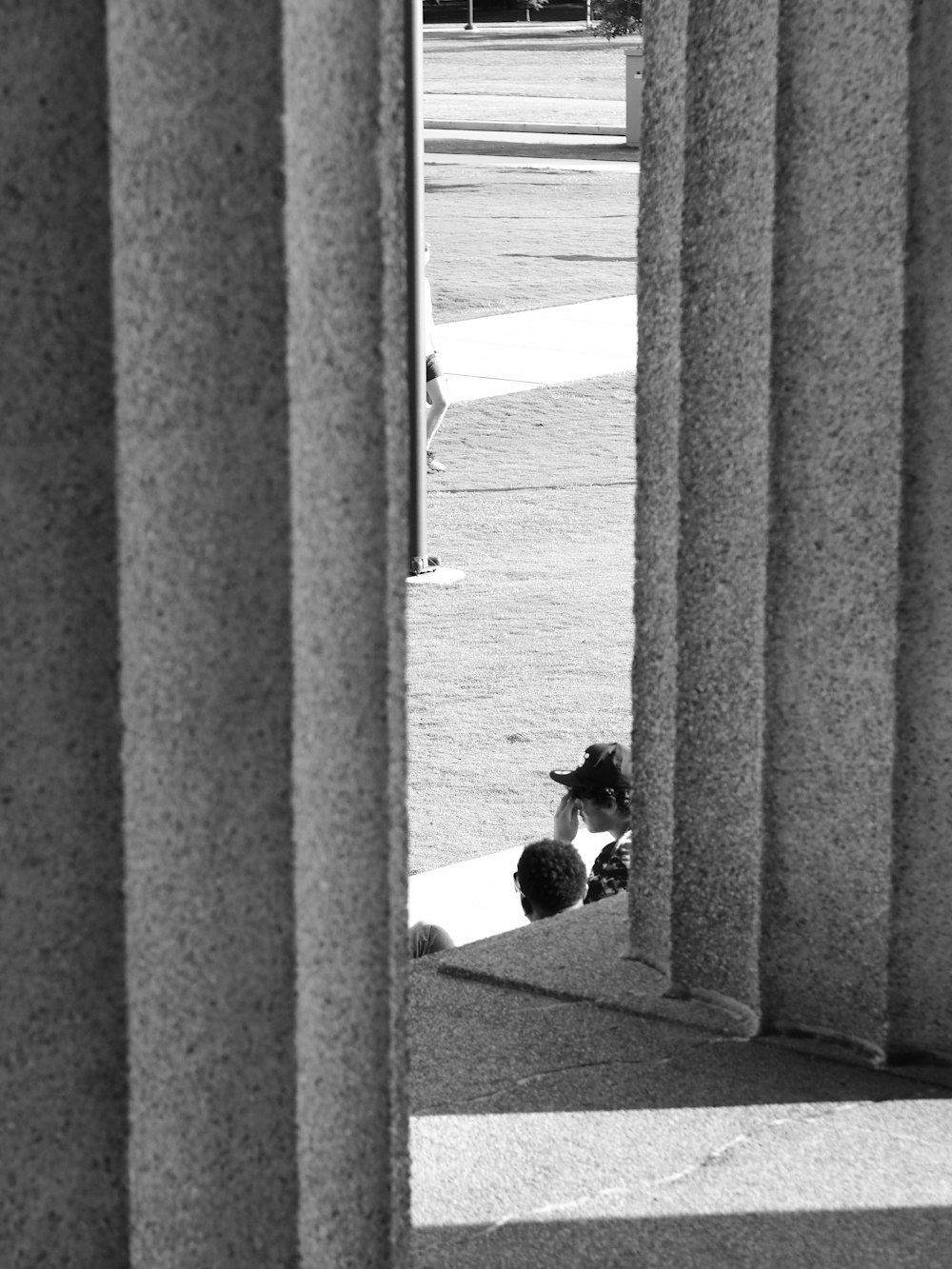 a black and white photo of a cat peeking out of a column