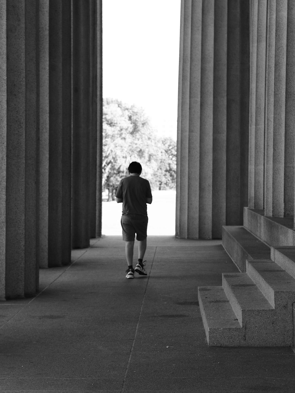 a man walking down a hallway between two large pillars