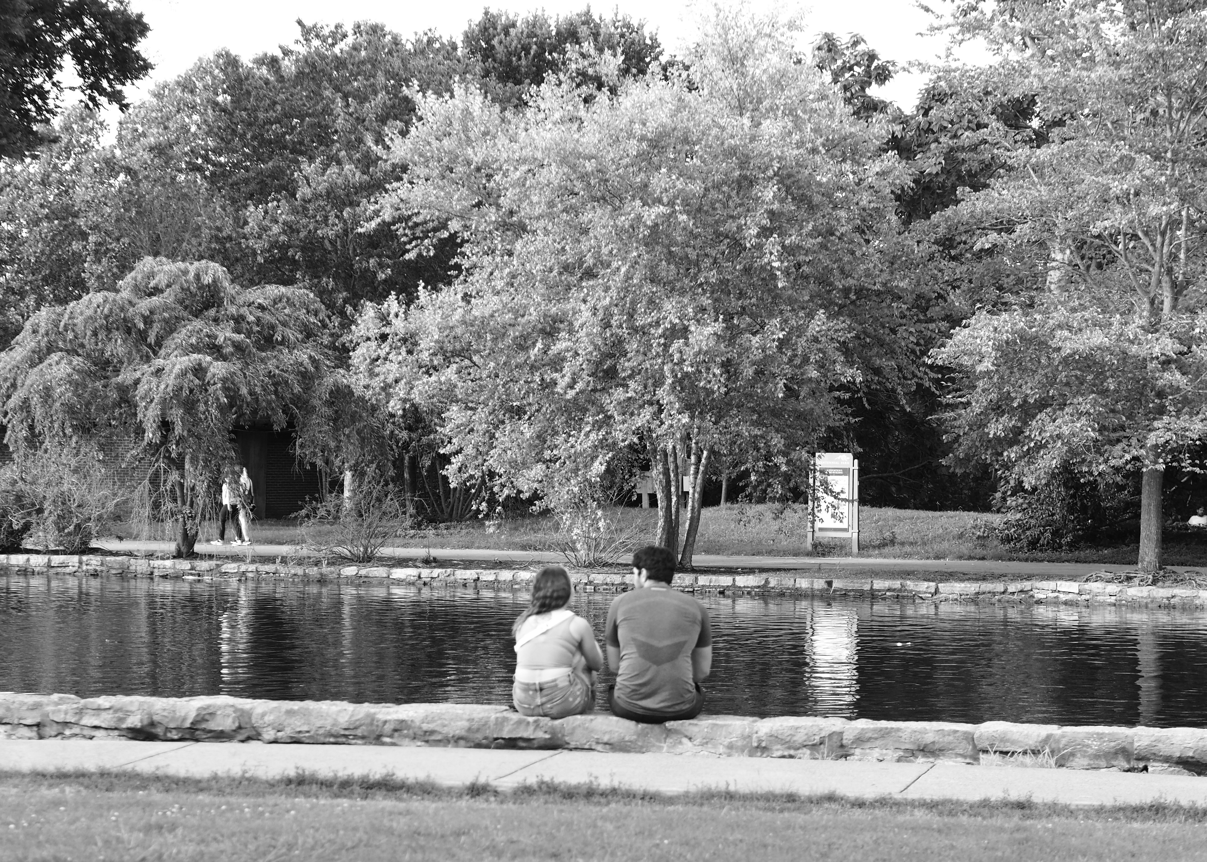 two people sitting on the edge of a pond