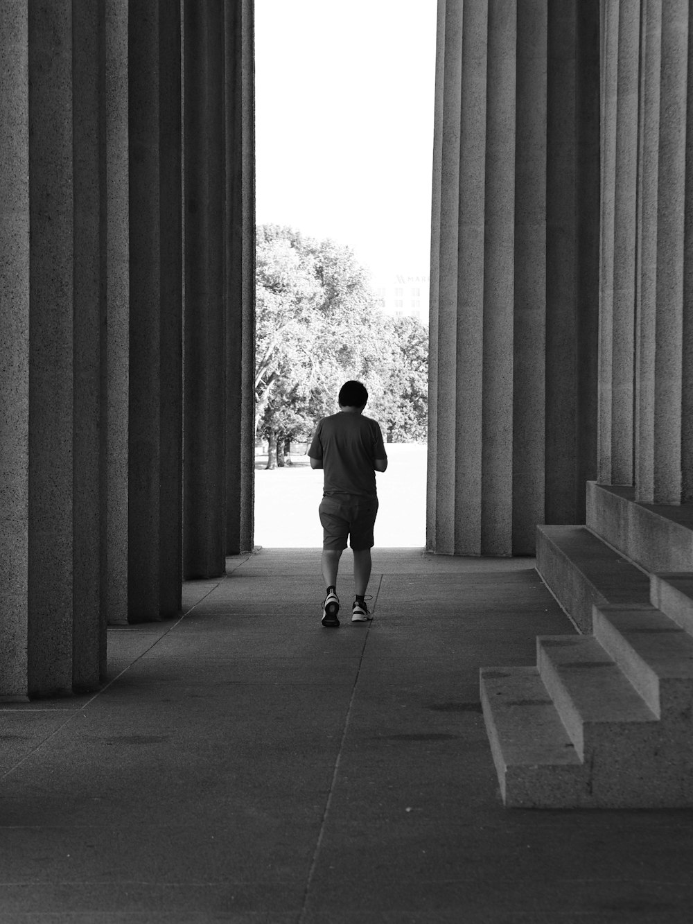 a man walking down a sidewalk next to tall pillars